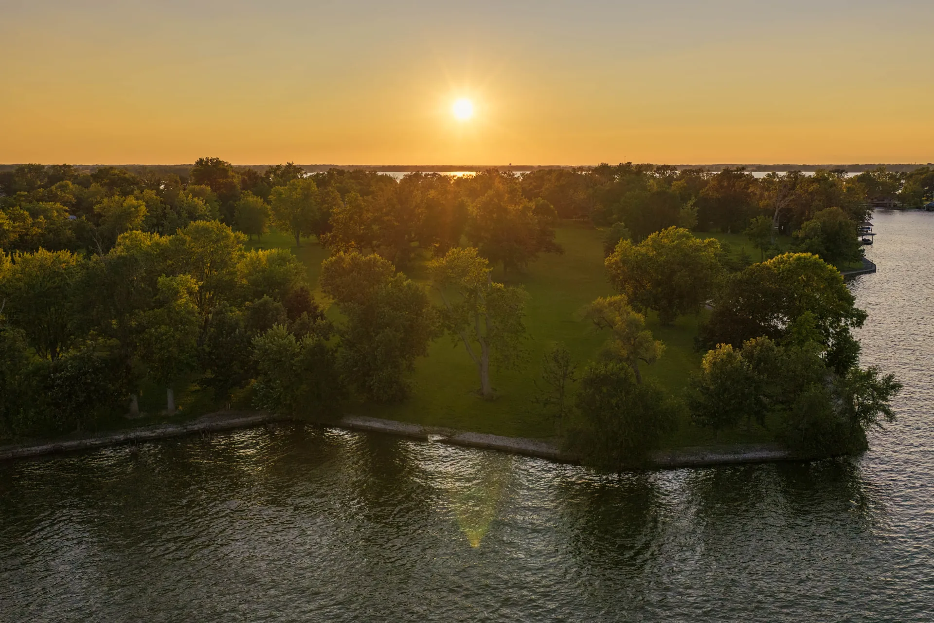 Aerial photograph at sunset of the wooded shoreline at The Orchard Reserve, with the sun setting over the open water of Indian Lake