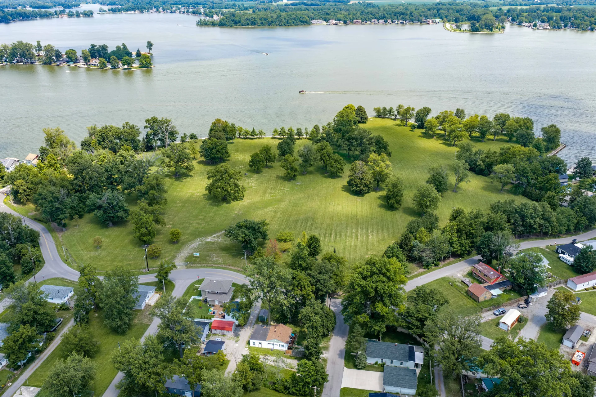 Low aerial photograph of the land at The Orchard Reserve, showing established trees, mown lawn and the water's edge beyond.